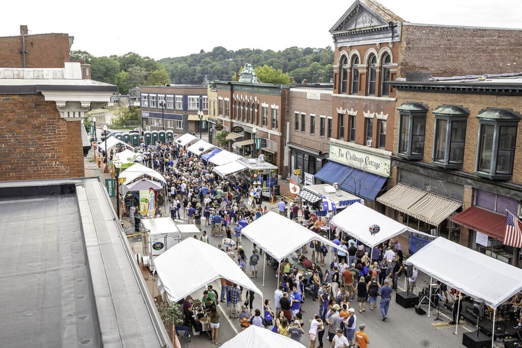 Crowds gather at a street festival with vendor tents among historic brick buildings